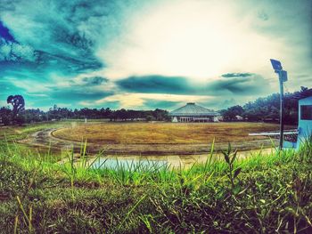 Grassy field against cloudy sky