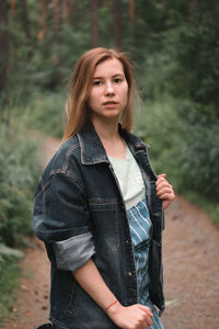 Portrait of young woman wearing denim jacket standing in forest
