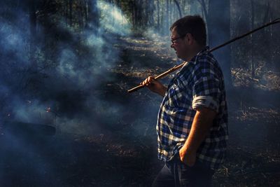 Side view of man with stick walking against trees in forest