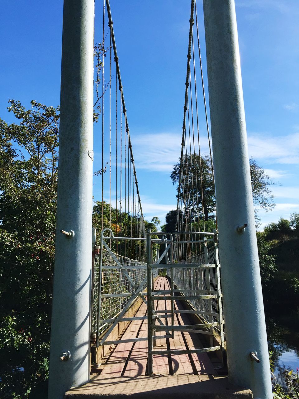 built structure, architecture, metal, sky, low angle view, blue, metallic, connection, engineering, bridge - man made structure, railing, tree, famous place, clear sky, travel destinations, sunlight, day, outdoors, suspension bridge, travel