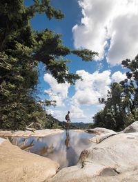 Man standing on rock by trees against sky