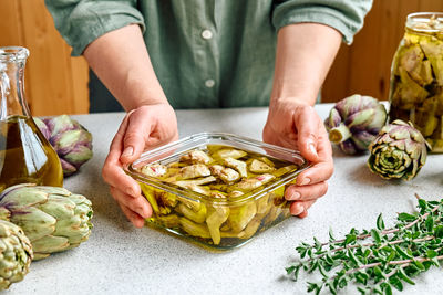 Artichoke hearts marinated with olive oil and herbs.woman holding glass bowl with pickled artichokes