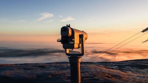 Close-up of coin-operated binoculars against sky during sunset