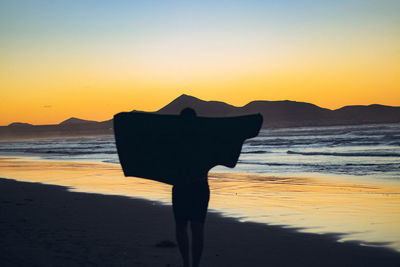 Rear view of woman standing at beach against sky during sunset