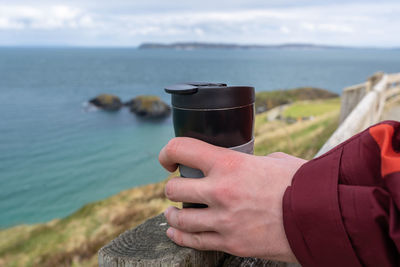 Midsection of man holding ice cream by sea against sky