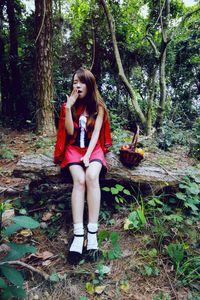 Full length of young woman sitting on fallen tree at forest