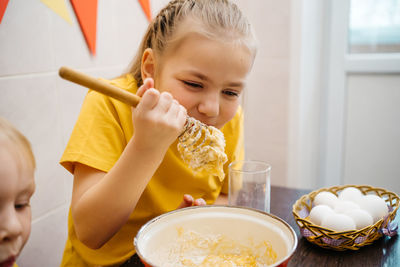 Girl with her brother cooks and tastes dough, white eggs on the table, easter holiday