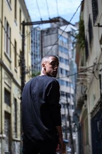 Portrait of young man standing amidst buildings in city