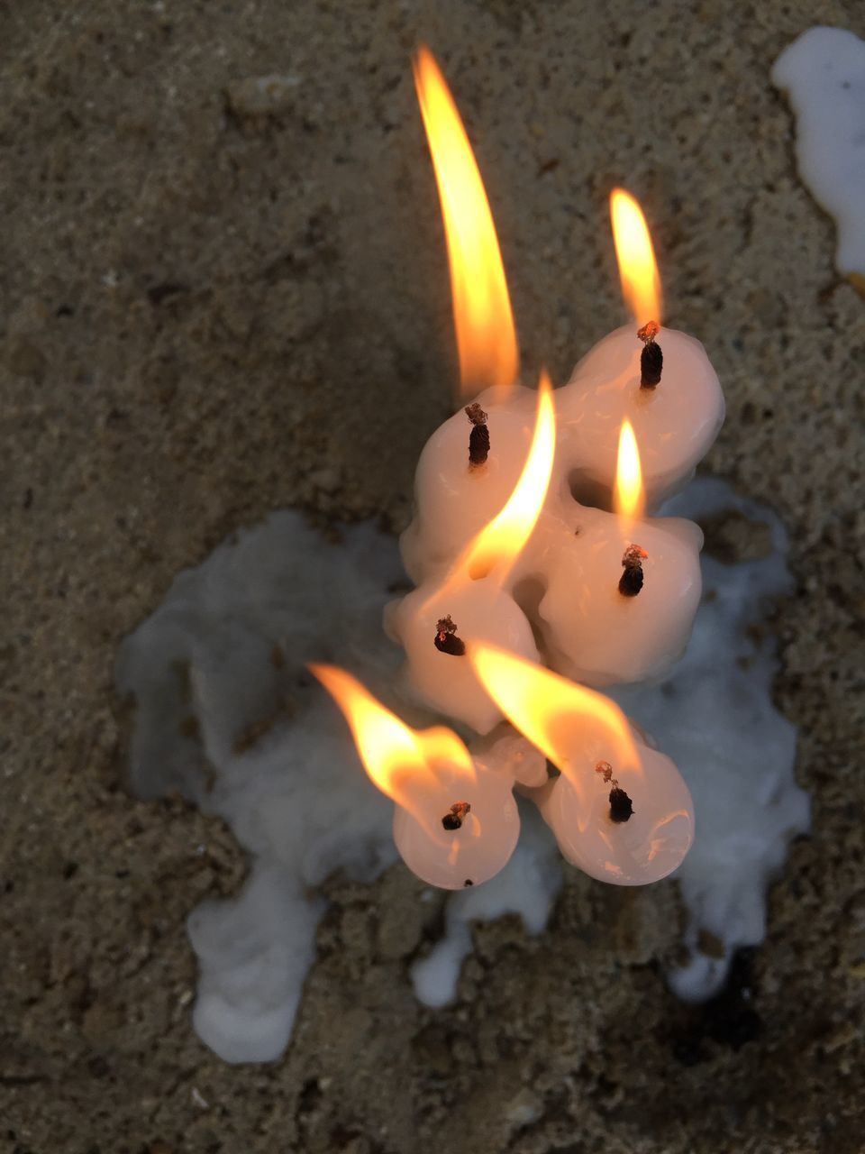 HIGH ANGLE VIEW OF LIT CANDLE IN SAND