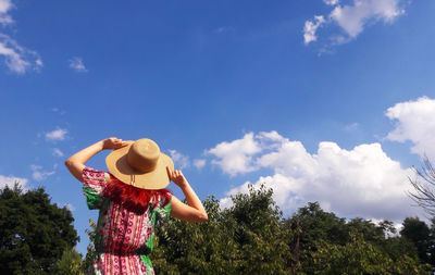 Low angle view of young woman standing against trees against sky