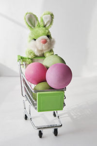 Toy soft green rabbit and  small shopping cart with colored natural chicken eggs. easter composition