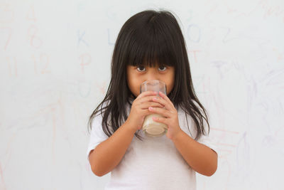 Portrait of a boy drinking glass against wall