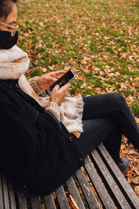Woman wearing mask using mobile phone while siting on bench at park