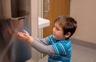 A young boy uses a air hand dryer to dry his hands after washing them in the bathroom sink.