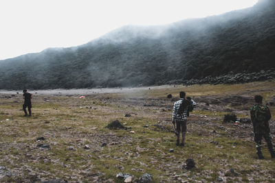 Rear view of people standing on field against mountain