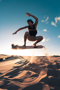 Man jumping at beach against sky during sunset