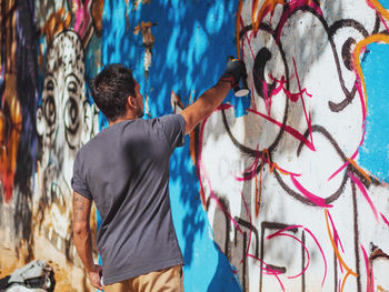 Rear view of young man spraying graffiti on wall