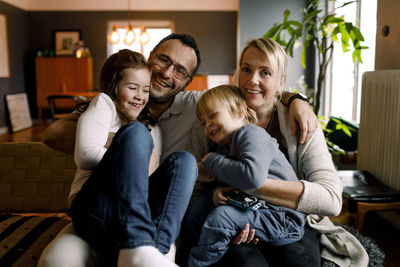 Portrait of parents with cheerful daughters sitting in living room at home