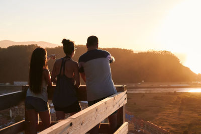 Rear view of people sitting on shore against sky during sunset