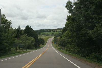 Empty road along trees and plants against sky
