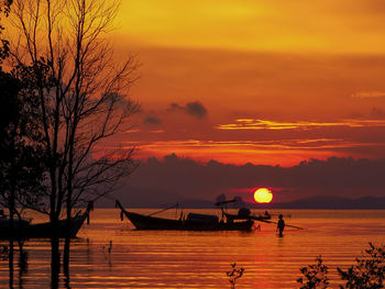 Silhouette boats in sea against orange sky
