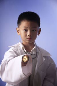 Portrait of boy wearing stethoscope and lab coat against wall