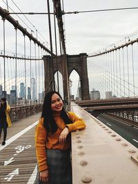 Young woman standing by bridge against sky in city