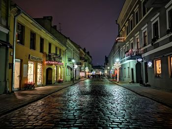 Wet street amidst buildings in city at night