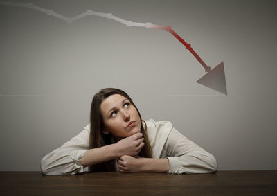 Portrait of young woman sitting on table against wall