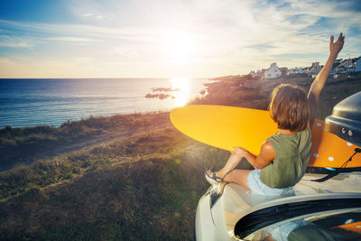 Rear view of woman standing in sea against sky during sunset