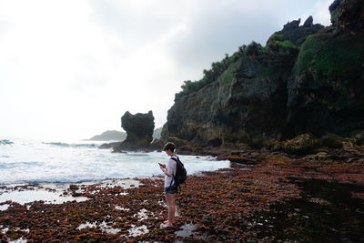 Man standing on rock by sea against sky