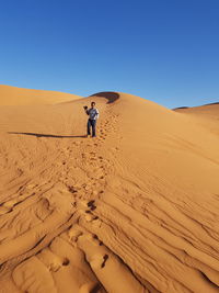 Man on sand dune in desert against clear blue sky