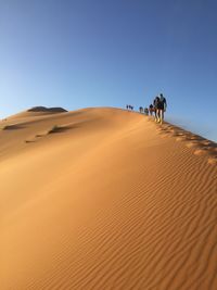 People walking on sand dune in desert against clear sky