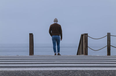 Rear view of man walking on pier against clear sky