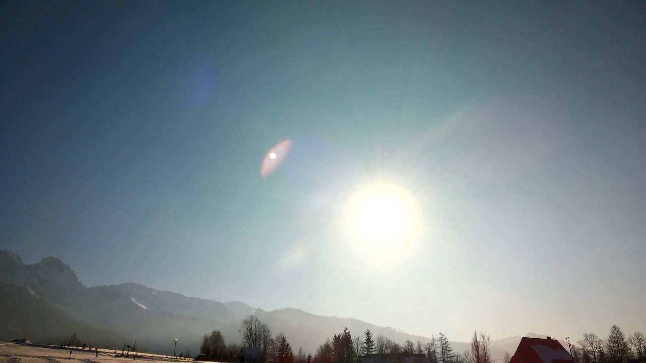 mountain, sun, clear sky, scenics, beauty in nature, tranquil scene, sunlight, tranquility, blue, sunbeam, copy space, nature, lens flare, tree, mountain range, sky, landscape, snow, low angle view, idyllic