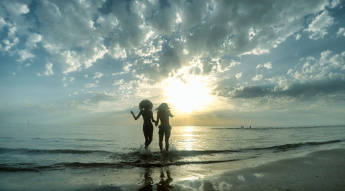 Friends standing on beach against sky during sunset