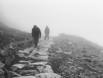 Full length of hikers walking on trail in foggy weather