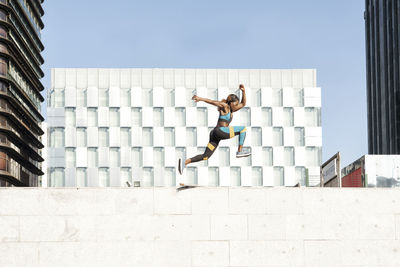 Young female athlete running on wall in city