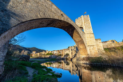 Low angle view of arch bridge over river against clear blue sky