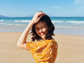 Side view of young woman sitting at beach against sky