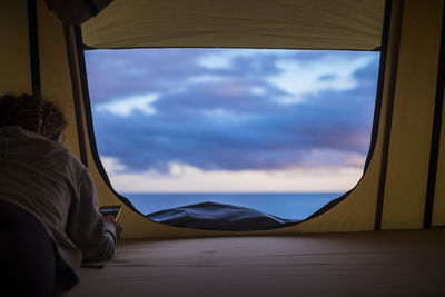 Woman using mobile phone while lying in tent against sea