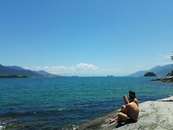 Friends sitting on rock against sea at beach