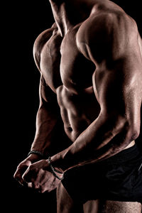 Midsection of shirtless man against black background