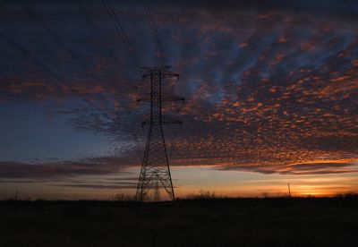 Silhouette electricity pylon against cloudy sky during sunset