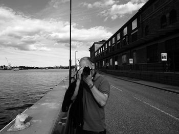 Man photographing while standing on road by sea against sky