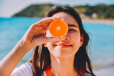 Close-up of smiling woman holding orange fruit at beach