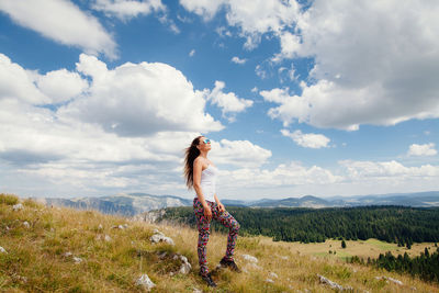 Full length of woman standing on field against cloudy sky