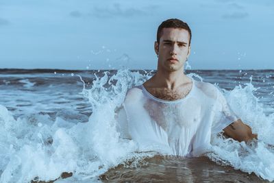 Portrait of young man splashing water in sea