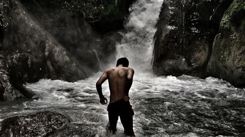 Rear view of shirtless man looking at waterfall