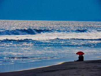 Rear view of person standing on beach against clear blue sky